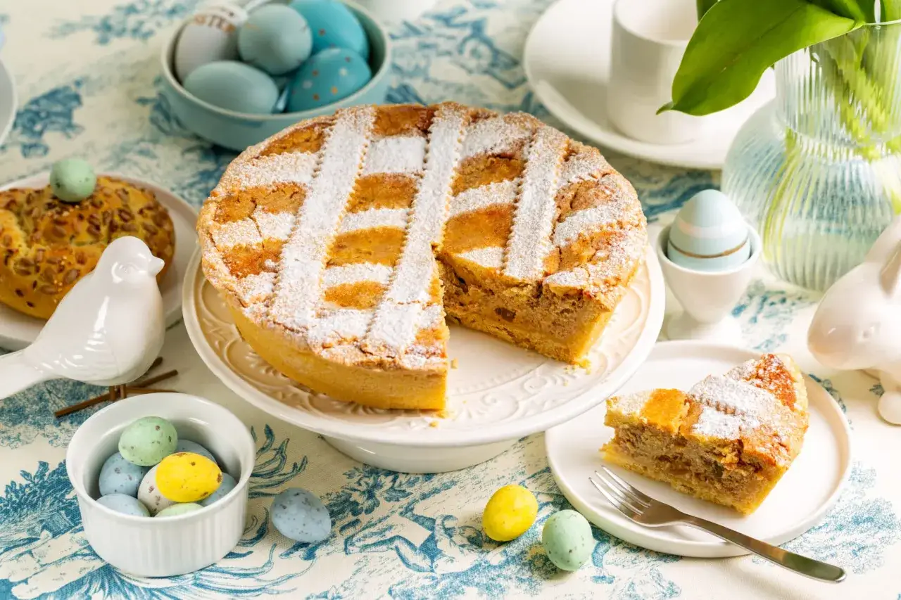 Une d&eacute;licieuse pastiera napoletana saupoudr&eacute;e de sucre glace, entour&eacute;e d'&oelig;ufs de P&acirc;ques color&eacute;s et d'une d&eacute;coration de lapin.