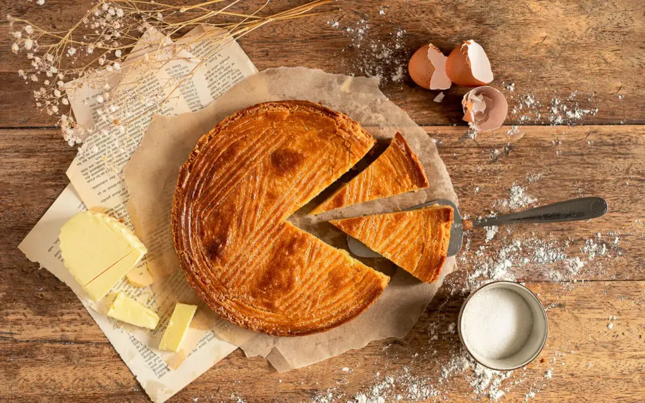 Un délicieux gâteau sablé breton, coupé en parts, avec du beurre, du sucre et des coquilles d'œufs sur une table en bois.