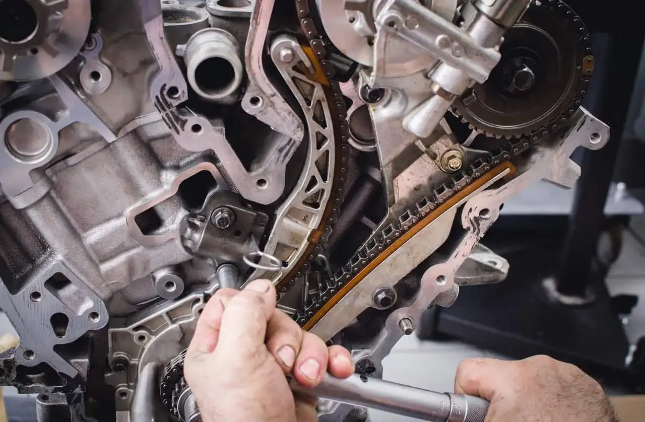 Mechanik naprawia uszkodzoną poduszkę silnika, pracując nad łańcuchem rozrządu i kołami zębatymi.