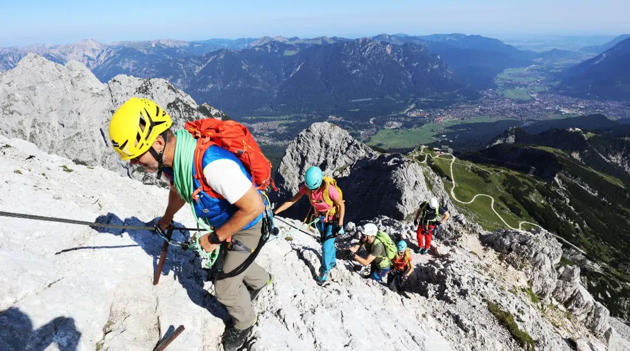 Bergsteiger sichern sich am Stahlseil auf dem **Alpspitz Klettersteig**. Die Gruppe genie&szlig;t die atemberaubende Aussicht auf das Tal.