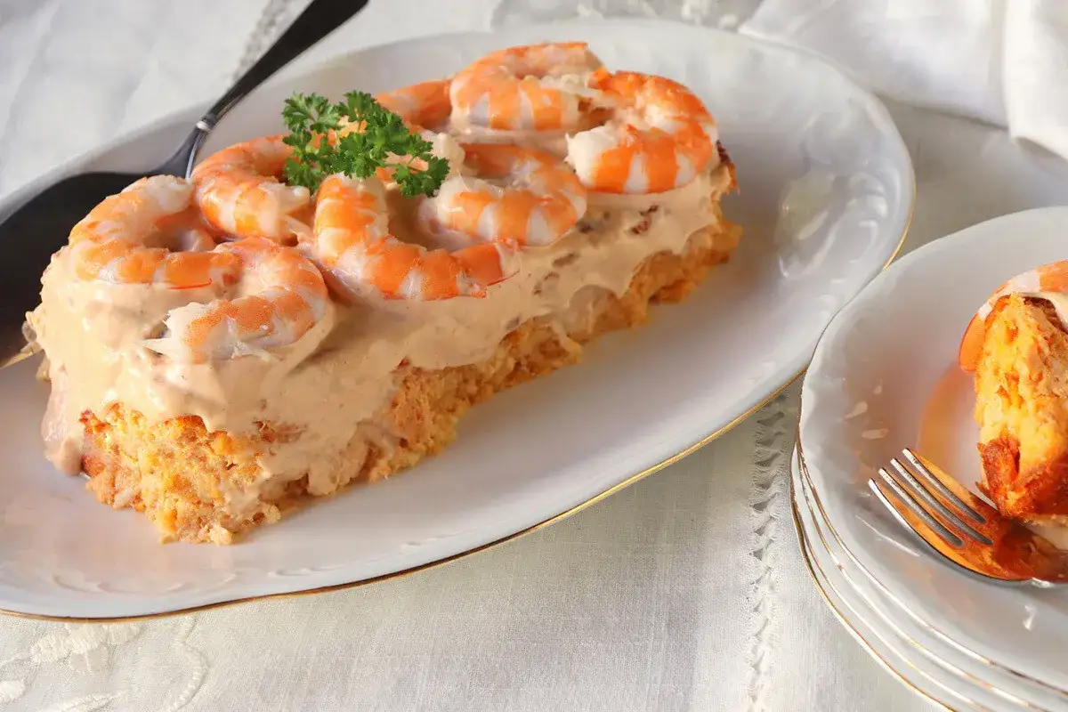 Pastel de pescado para Navidad, cubierto con una cremosa salsa rosada y adornado con gambas. Un entrante festivo y delicioso.