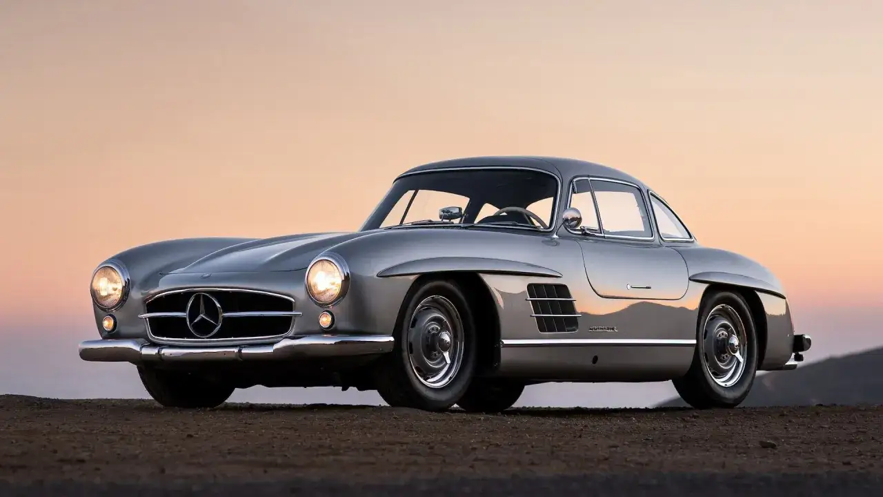 Srebrny Mercedes Gullwing z charakterystycznymi drzwiami, zaparkowany na pustkowiu o zachodzie słońca.