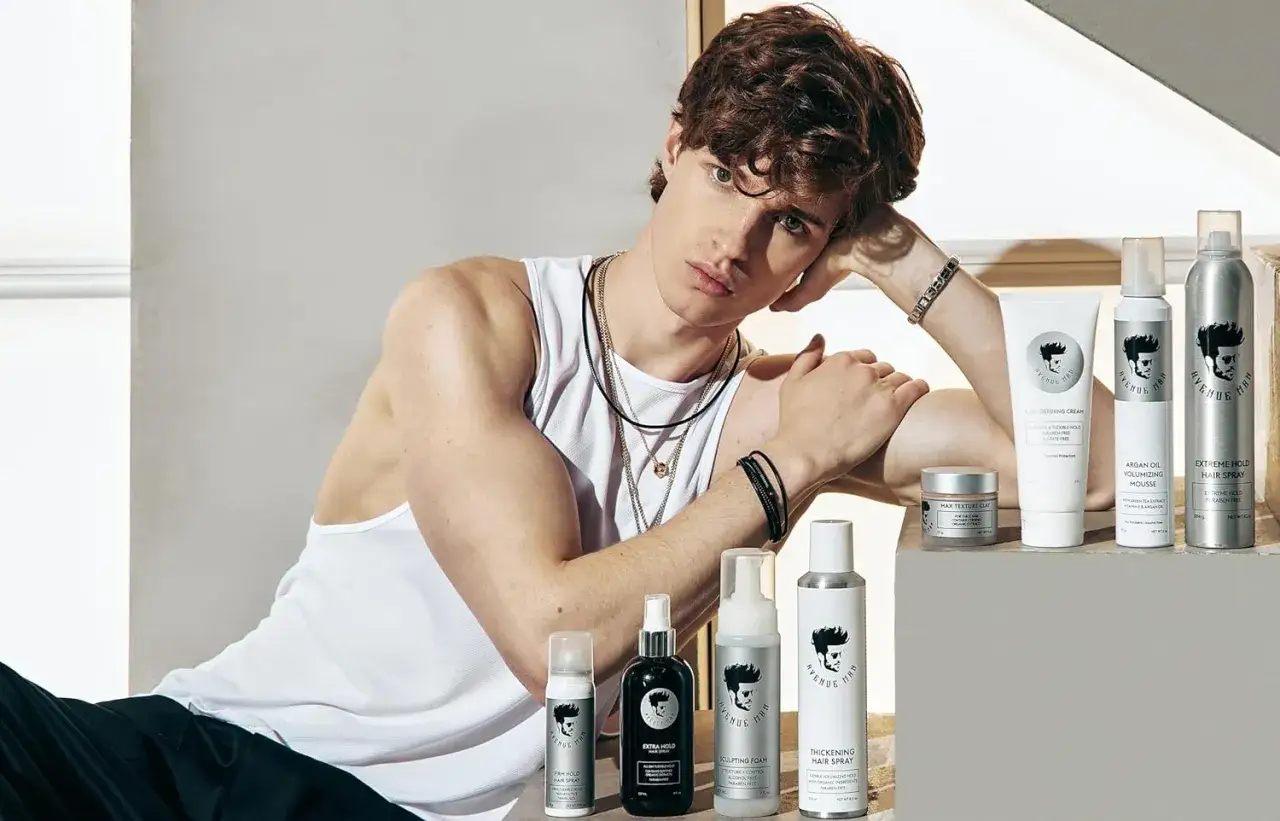 Joven con peinado rizos hombre, apoyado en su brazo, rodeado de productos para el cabello.