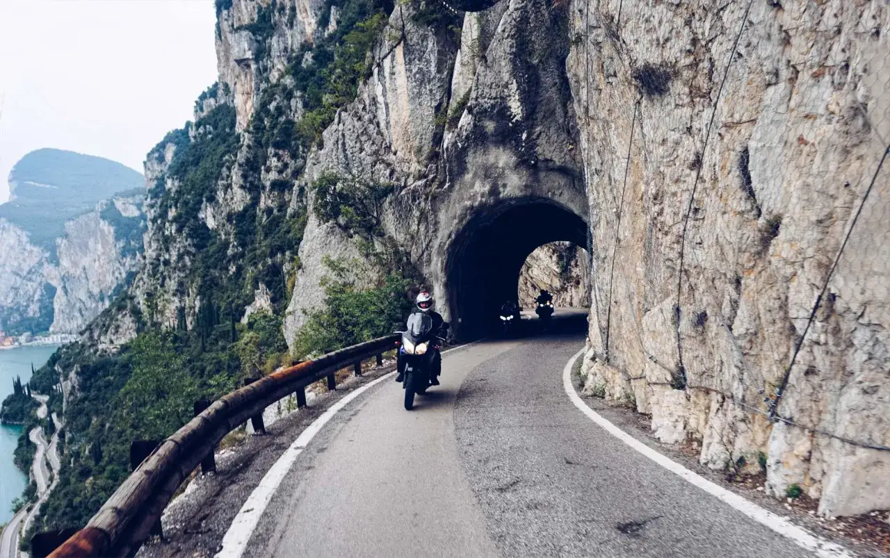 Motocykliści przemierzają malowniczą strada della forra, wjeżdżając do skalnego tunelu.