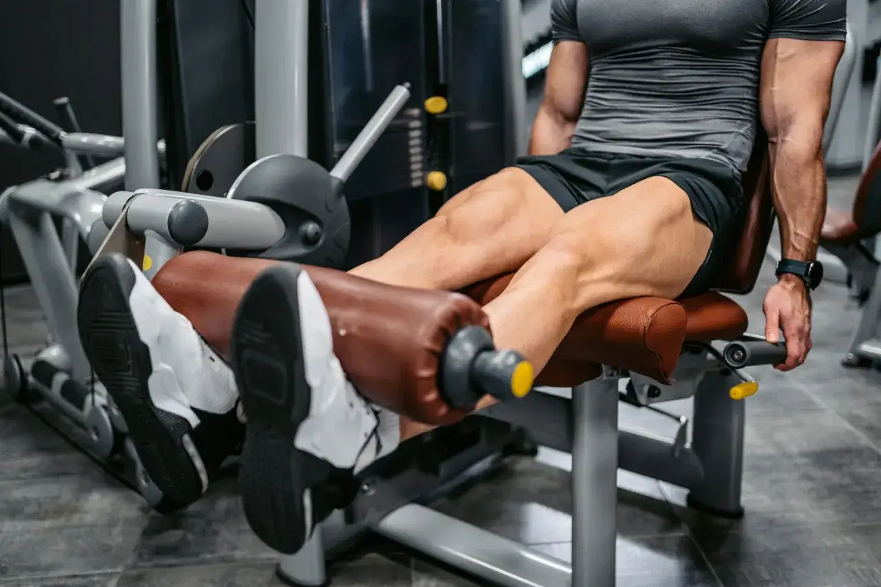Un homme musclé effectue un exercice quadriceps sur une machine de musculation, concentré sur son entraînement.