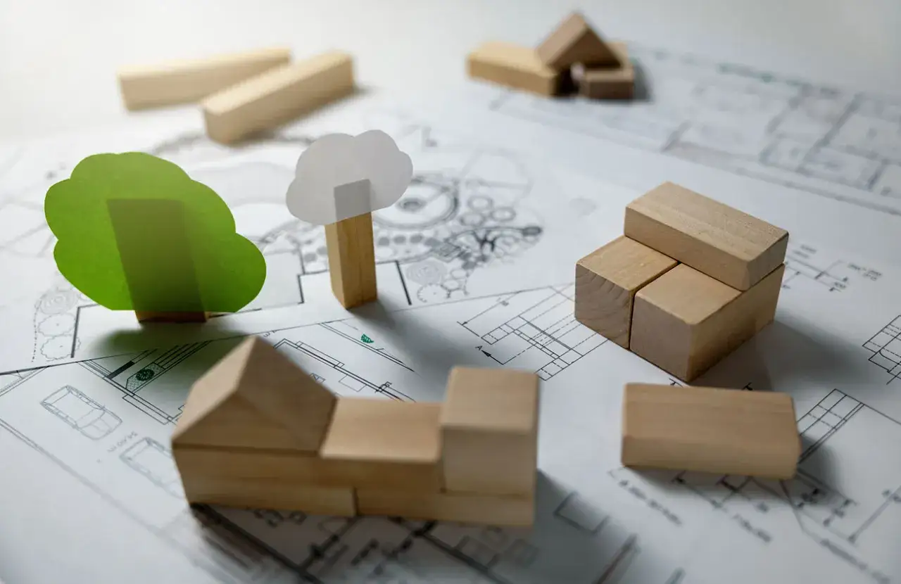 Maqueta de casa y &aacute;rboles sobre planos, buscando c&oacute;mo abaratar costes en el dise&ntilde;o.