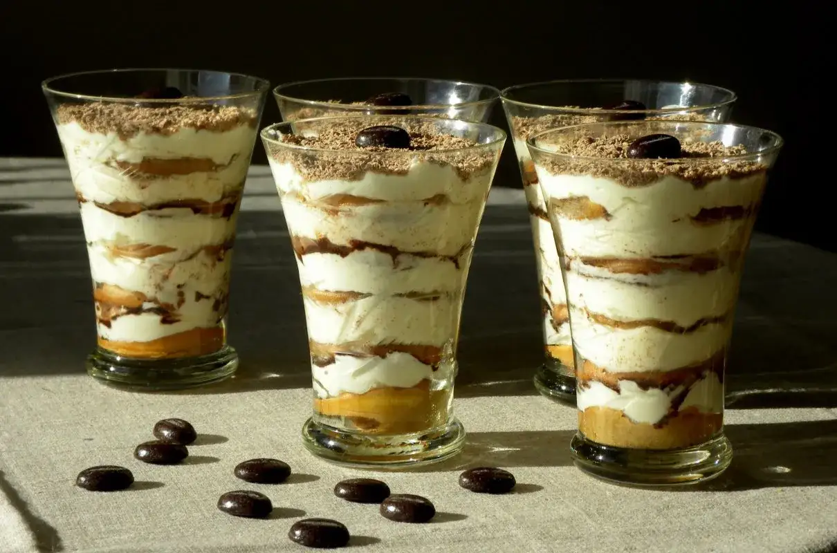 Pyszne tiramisu w pucharkach, warstwowo ułożone z kremem i biszkoptami, posypane kakao i kawą.