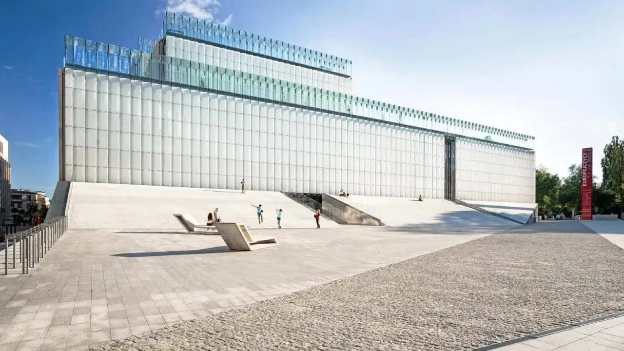 Nowoczesny budynek z przeszklonym dachem i białymi panelami, z ludźmi odpoczywającymi na schodach. Plac teatralny Lublin.