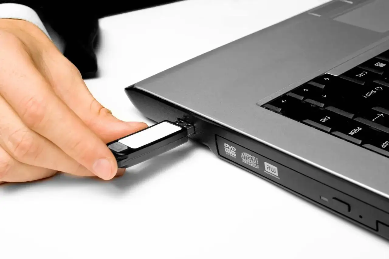 Dłoń wkłada pendrive do laptopa, pokazując, jak znaleźć pendrive na laptopie.