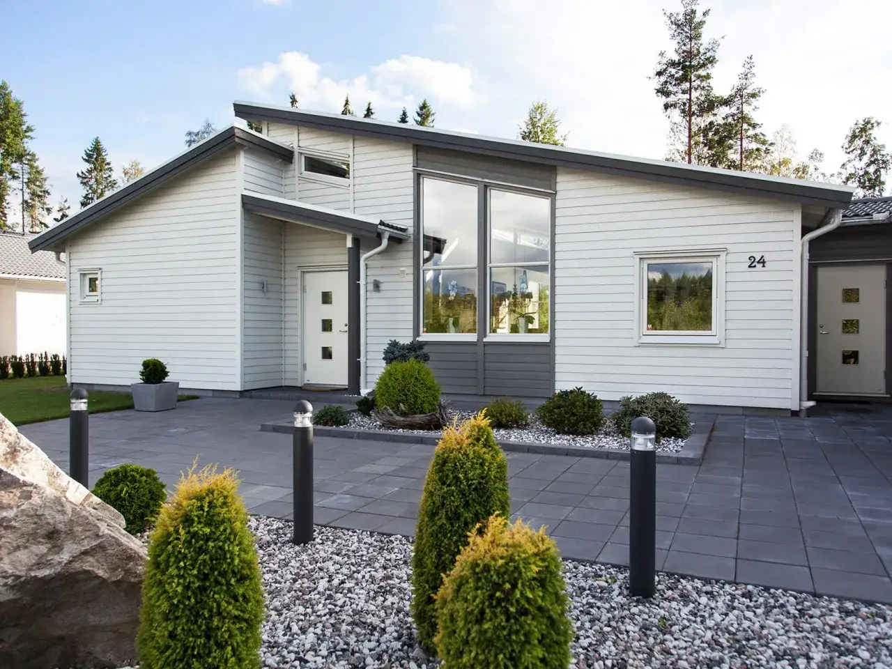 Modern villa med stora f&ouml;nster och en inbjudande entr&eacute;. Perfekt inspiration framsida hus med stenl&auml;ggning och gr&ouml;na buskar.