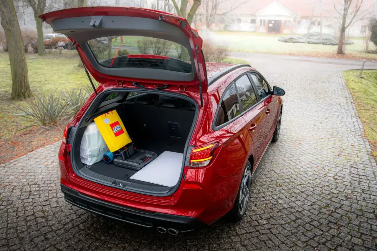 Czerwony Hyundai i30 Wagon z otwartym bagażnikiem, w którym widać torbę z logo LEGO, narzędzia i białą płytę.