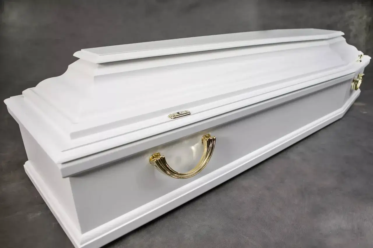 Elegancka, biała trumna z ozdobnymi złotymi uchwytami. Jej prosta forma i jasny kolor symbolizują spokój i godność.