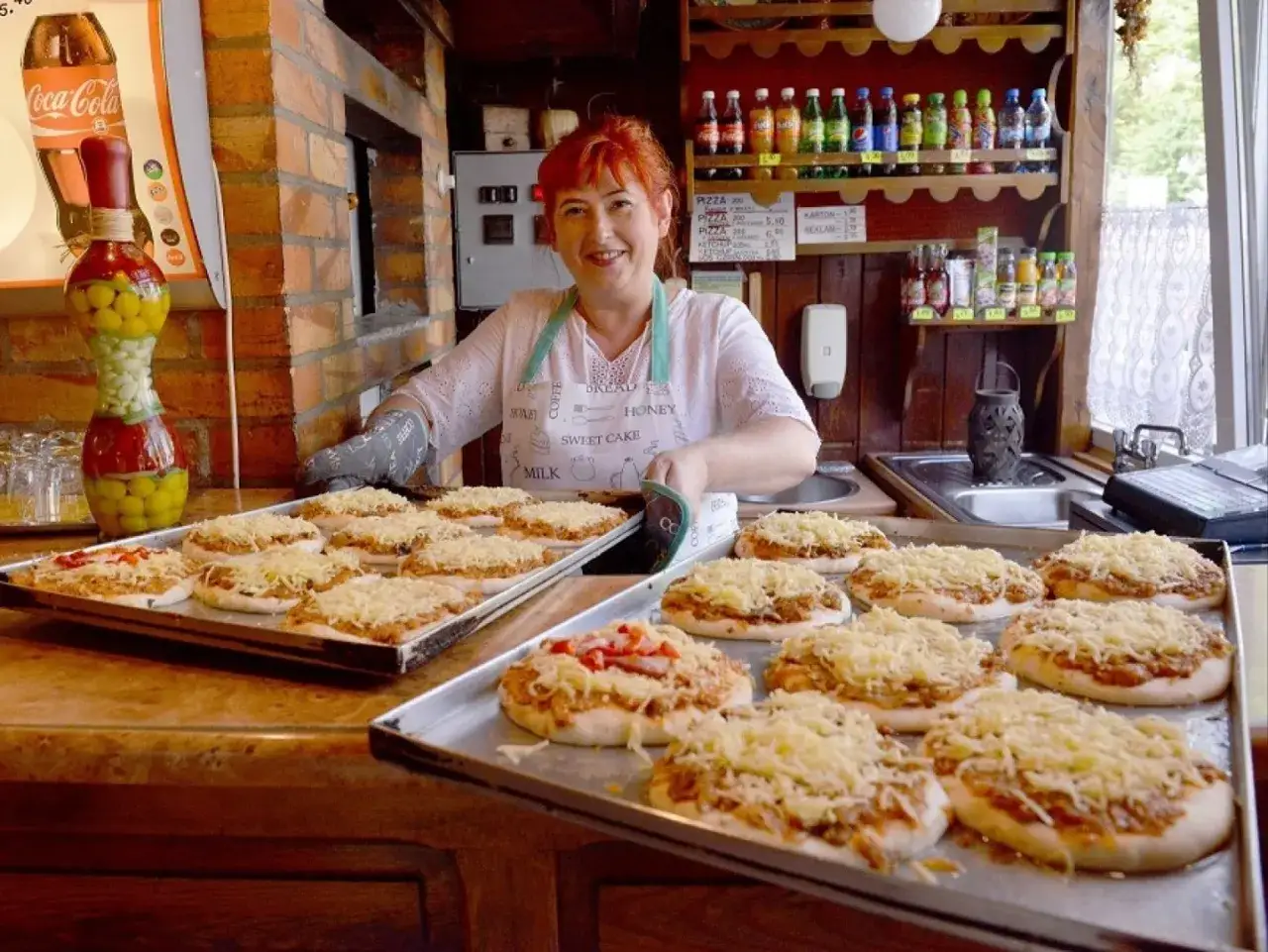 Kobieta w fartuszku przygotowuje pizze w najstarszej pizzerii w Polsce. Na tacach leżą gotowe do pieczenia placki z serem.