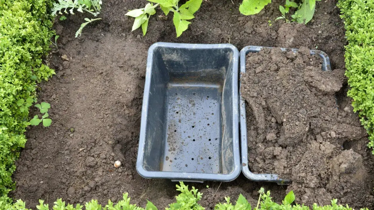 Gartenarbeit: Eine schwarze Wurzelsperre wird in die Erde eingesetzt, um die Ausbreitung von Minze zu verhindern. Daneben liegt aufgeworfene Erde.