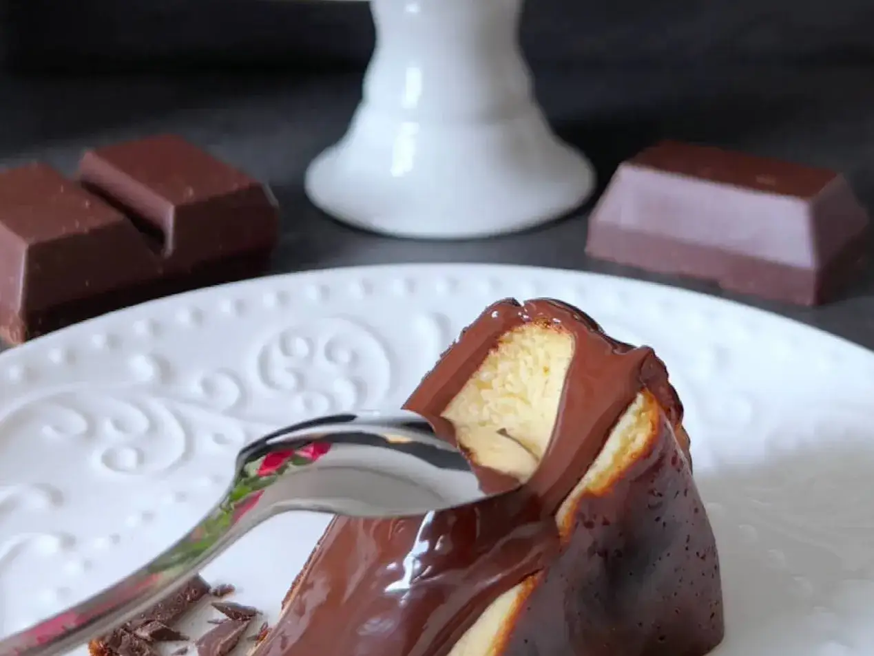 Una fetta di cheesecake basca con glassa al cioccolato fondente, pronta per essere gustata.