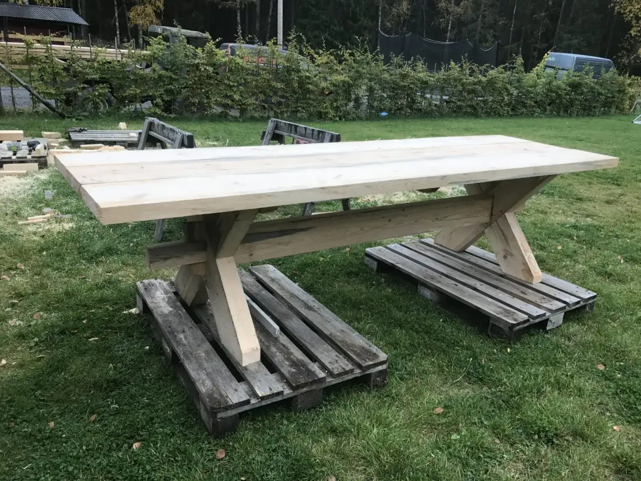 Ett grovt, hemmabyggt matbord i trä står på pallar utomhus. Perfekt för den som vill bygga eget matbord.