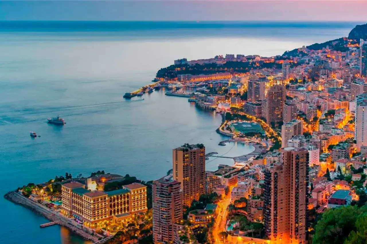 Vista panoramica di Montecarlo al tramonto, con il porto, yacht e la citt&agrave; illuminata. Ecco cosa vedere a Montecarlo: lusso e mare.