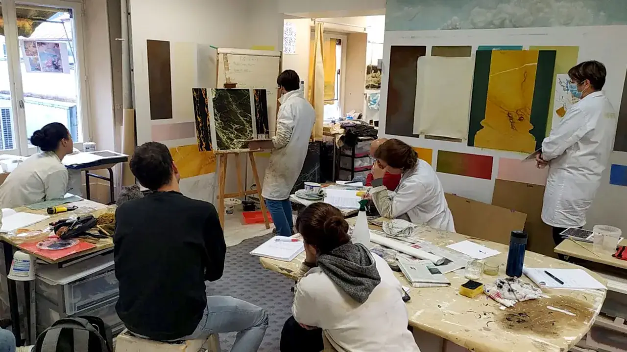 Des élèves attentifs dans une école d'art, observant une démonstration de techniques de peinture sur des toiles.