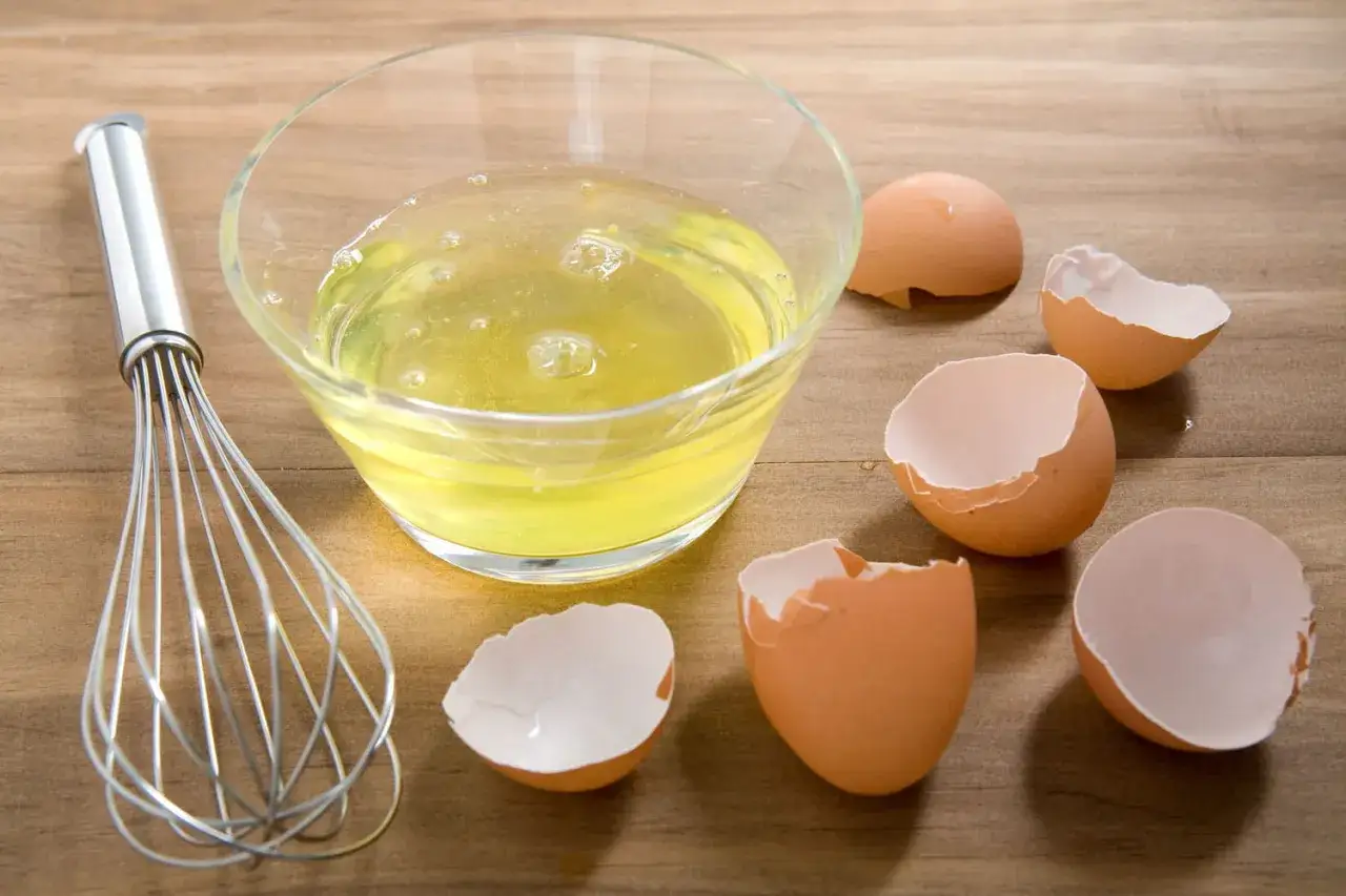 Un fouet et un bol de blancs d'œufs, entourés de coquilles vides. Parfait pour savoir que faire avec des blancs d'œufs : meringues ou financiers !