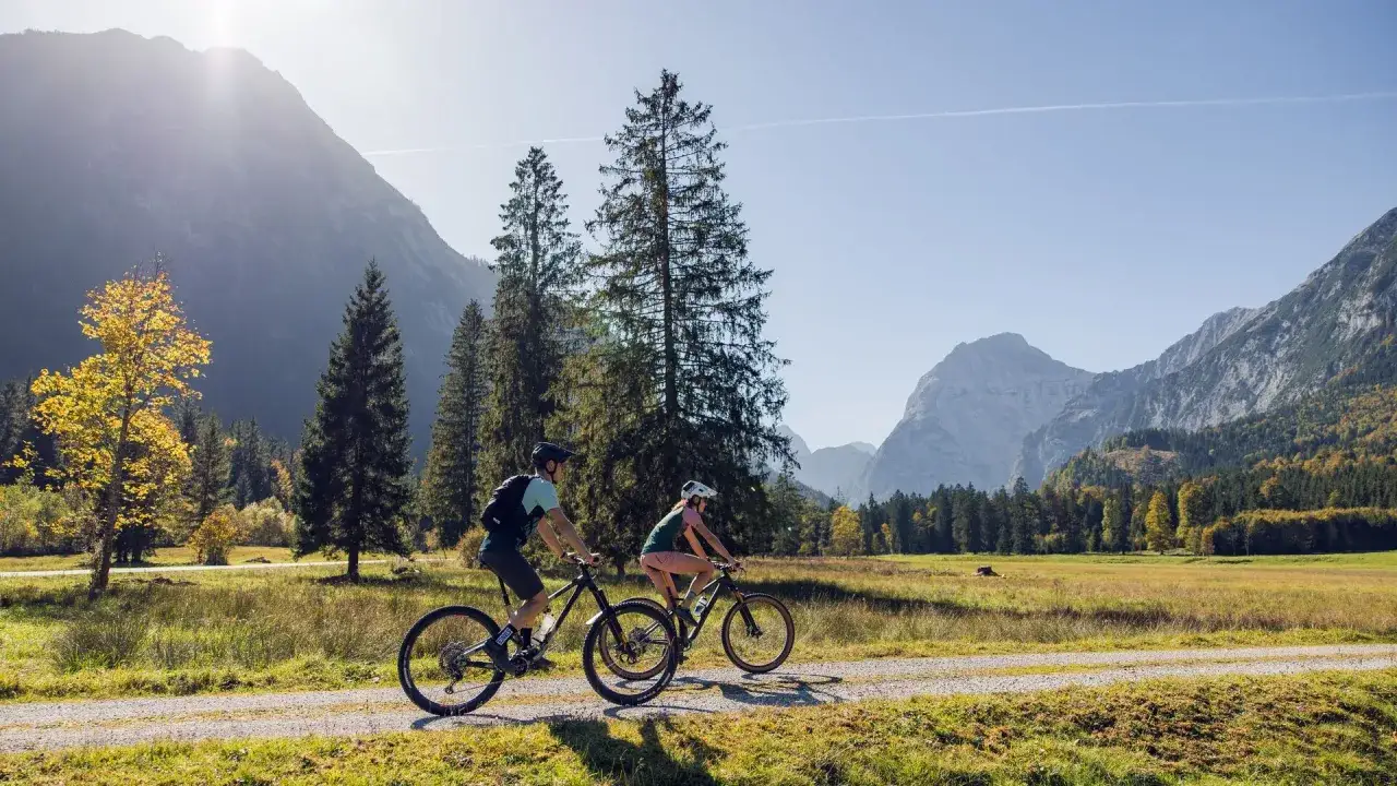 Para rowerzyst&oacute;w przemierza malownicze trasy rowerowe w Austrii, otoczeni jesiennymi krajobrazami i majestatycznymi g&oacute;rami.