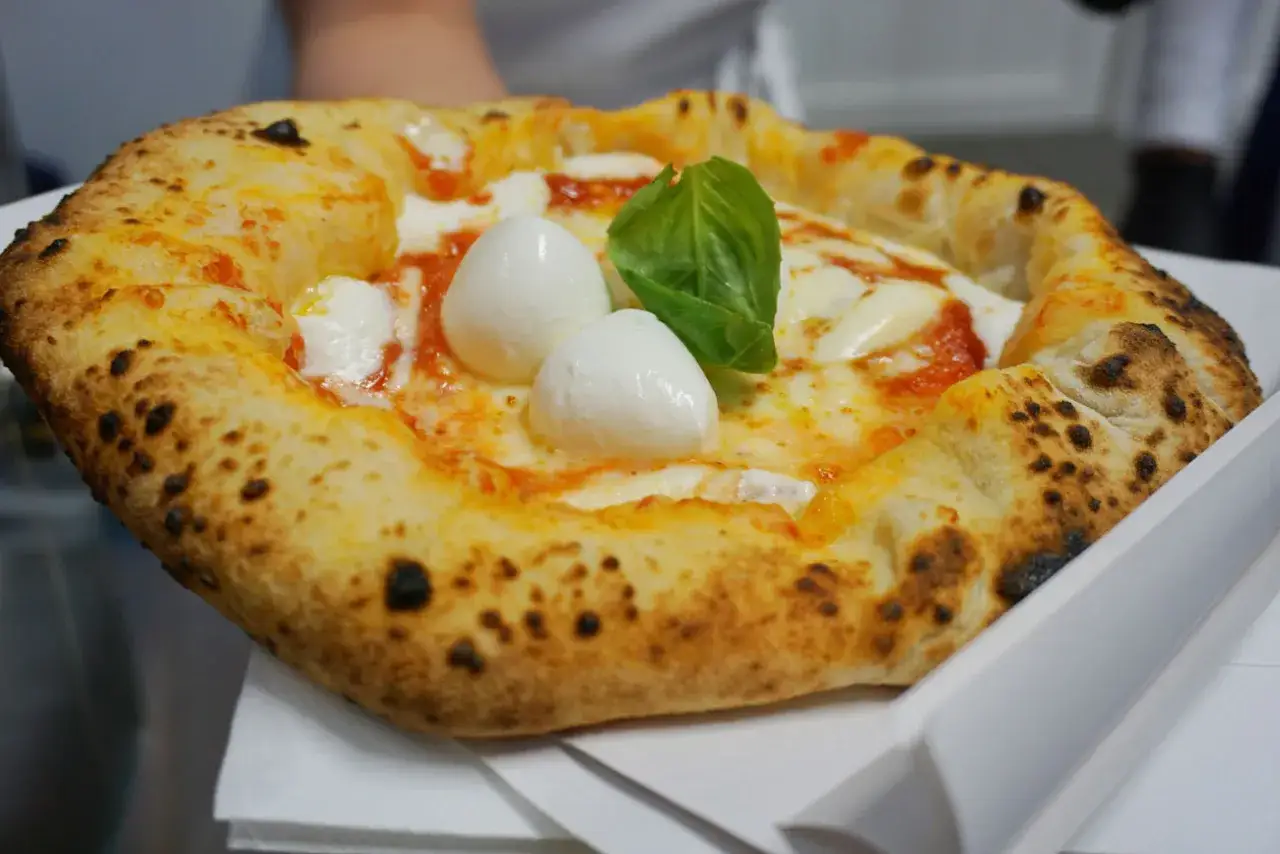 Pizza Margherita, uno dei piatti tipici napoletani, con mozzarella di bufala filante e basilico fresco.