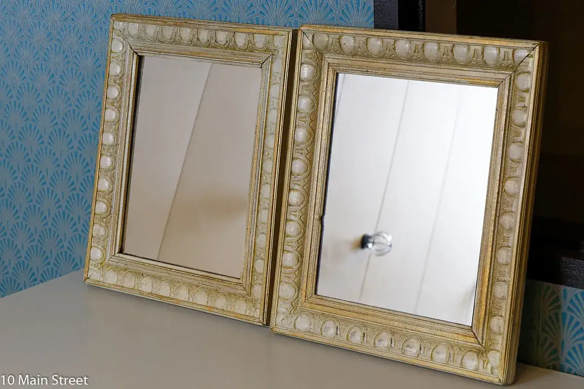Deux miroirs avec un encadrement fait maison, relooké avec une finition dorée et texturée, sur un fond bleu à motifs.