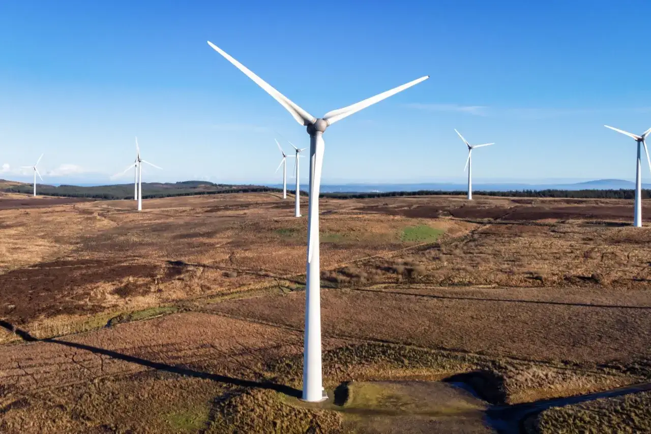 Weite Landschaft mit mehreren weißen onshore Windkraftanlagen unter blauem Himmel.