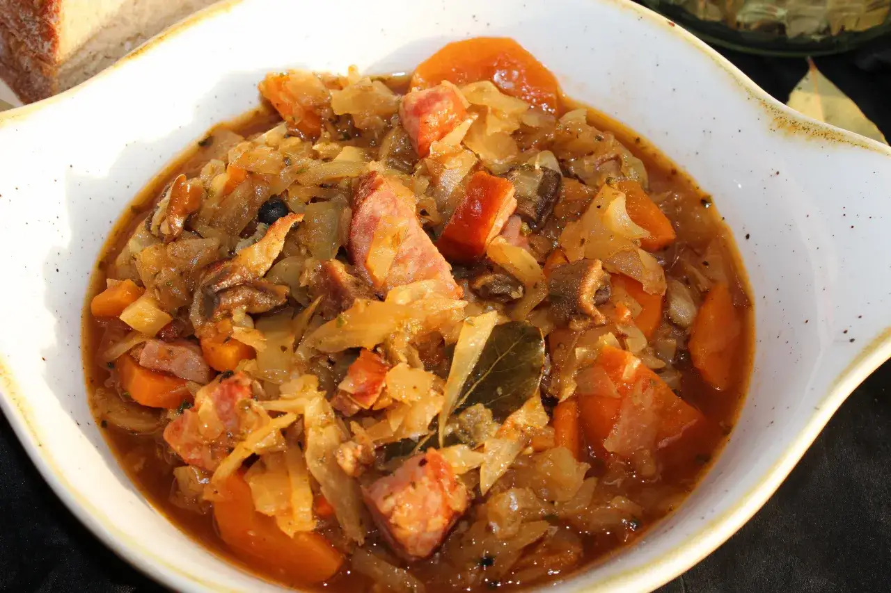Pyszny bigos ze słodkiej kapusty z kawałkami kiełbasy i marchewki, podany w białej misie.