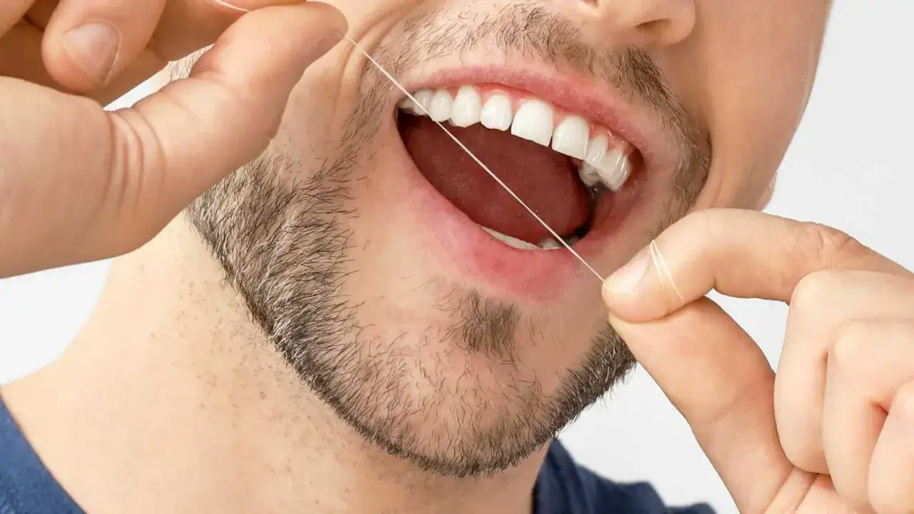Mężczyzna czyści zęby nicią dentystyczną, dbając o higienę jamy ustnej. To ważny krok w profilaktyce, szczególnie gdy zęby są ruszające się.