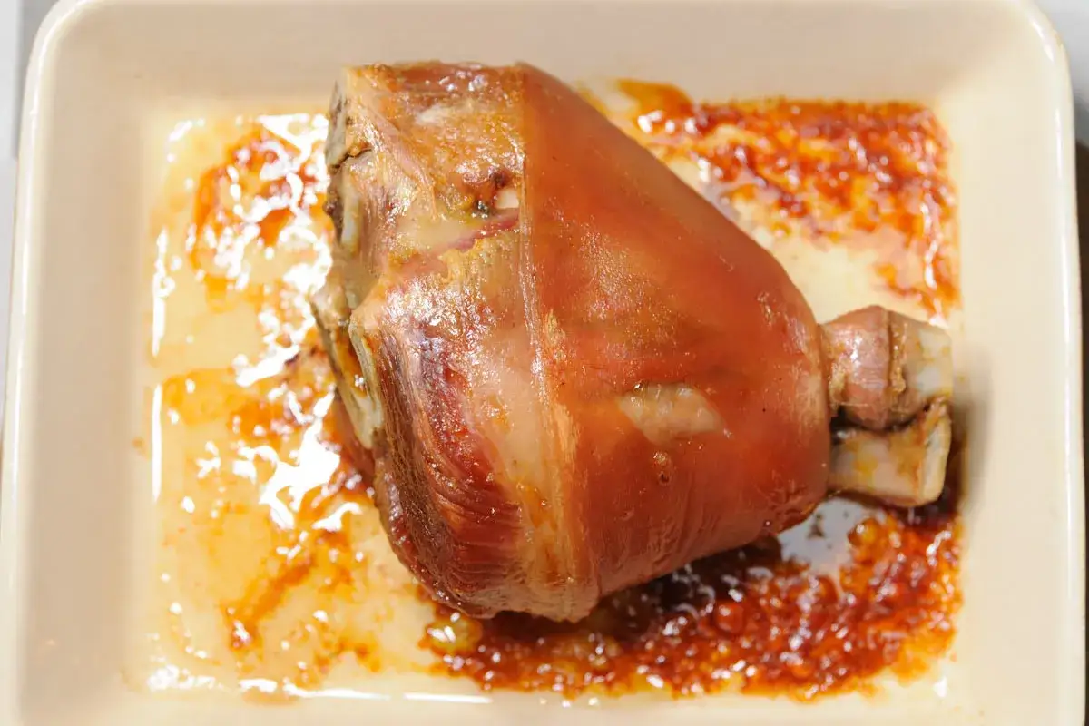 Un jarret de porc demi-sel doré, prêt pour la cuisson, baignant dans son jus savoureux dans un plat en céramique.