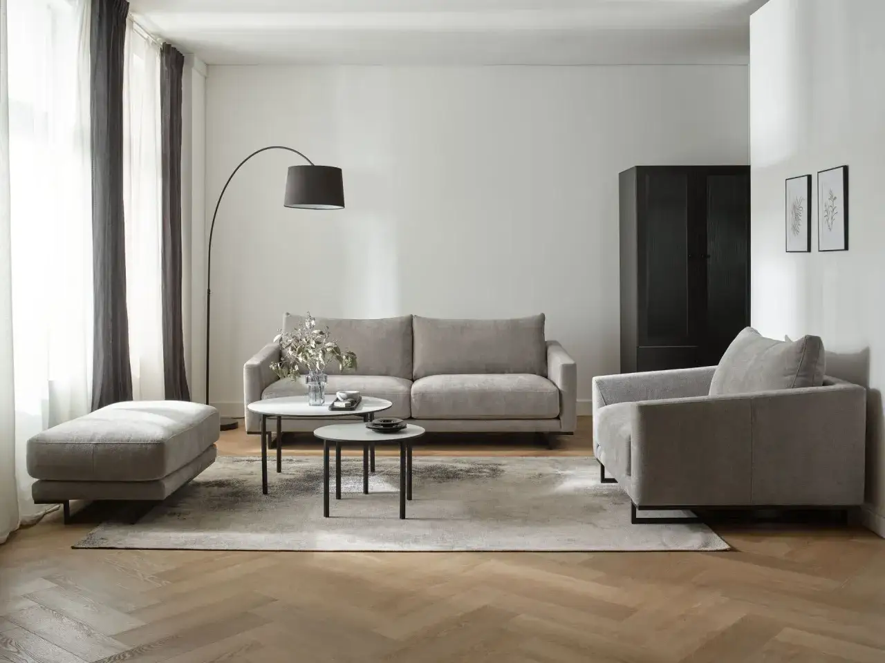 Nowoczesny salon z dwiema sofami, fotelem i pufą. W centrum dwie okrągłe ławy.