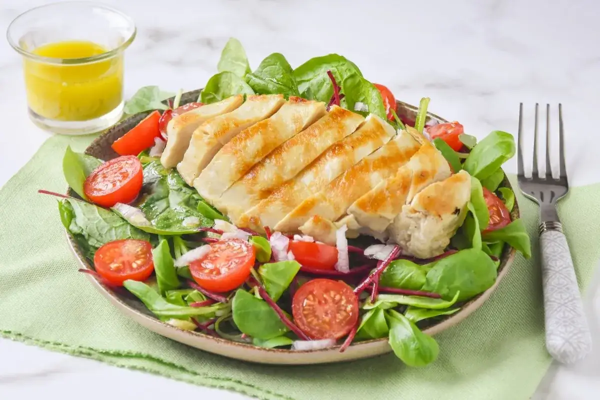 Deliciosa ensalada de pollo a la parrilla con tomates cherry, hojas verdes y aderezo.
