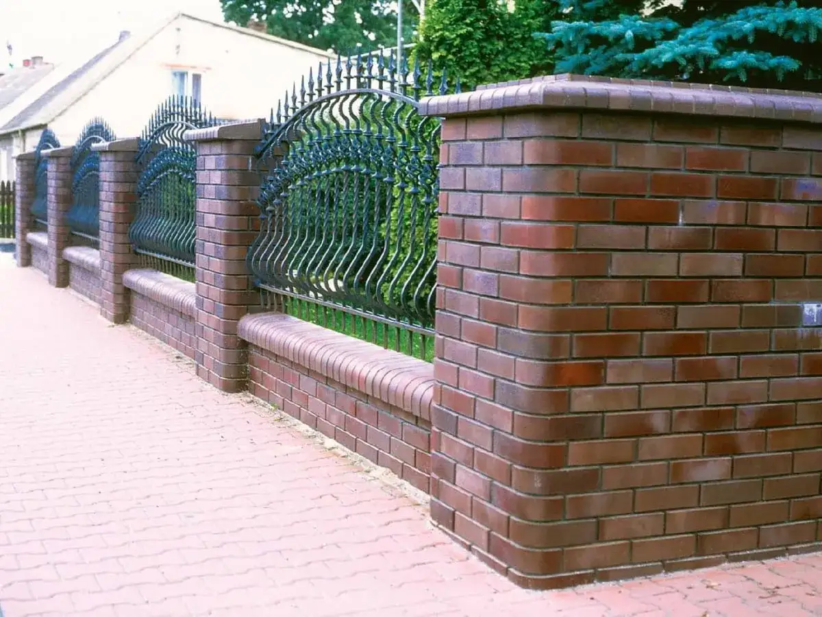 Solidne ogrodzenie z cegły z ozdobnym kutym metalowym przęsłem, tworzące elegancką granicę posesji.
