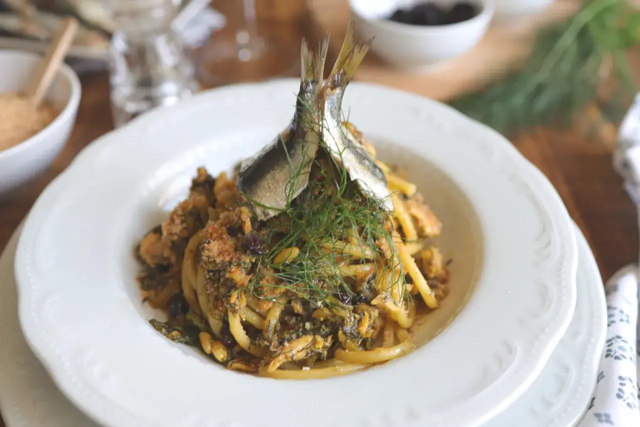Un piatto di pasta con le sarde, guarnito con finocchietto fresco e due pesciolini interi.