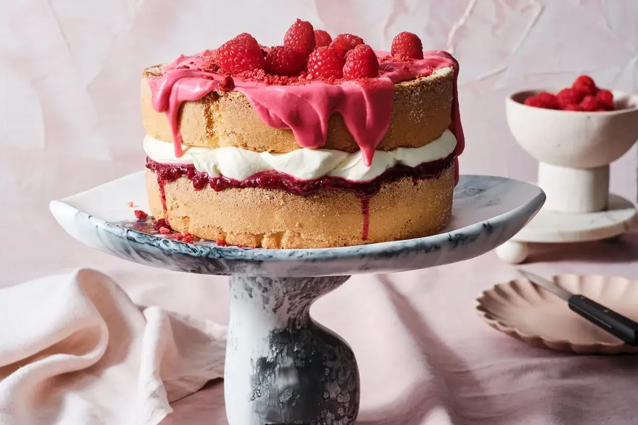 Un d&eacute;licieux victoria sponge cake, garni de cr&egrave;me, de confiture de framboises et de framboises fra&icirc;ches, avec un gla&ccedil;age rose d&eacute;goulinant.