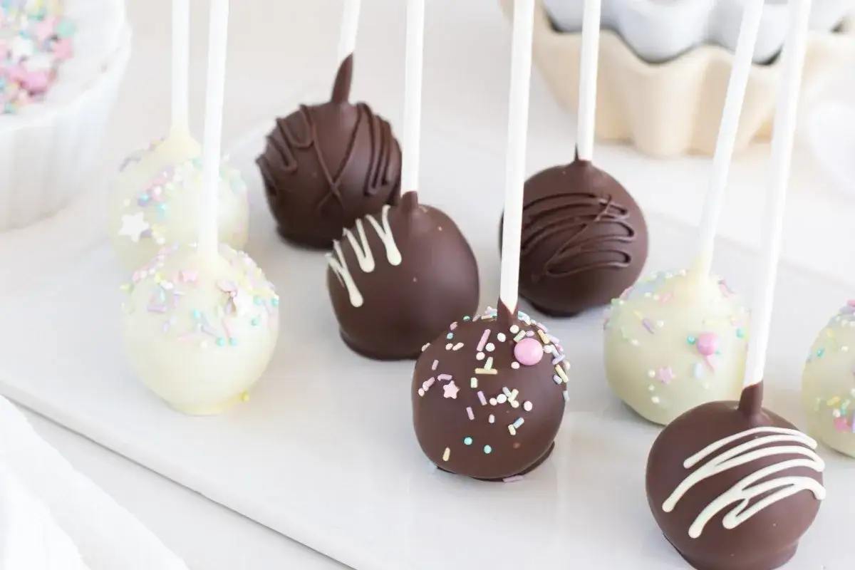 Deliciosos cake pops cubiertos de chocolate blanco y oscuro, decorados con chispas de colores y glaseado.