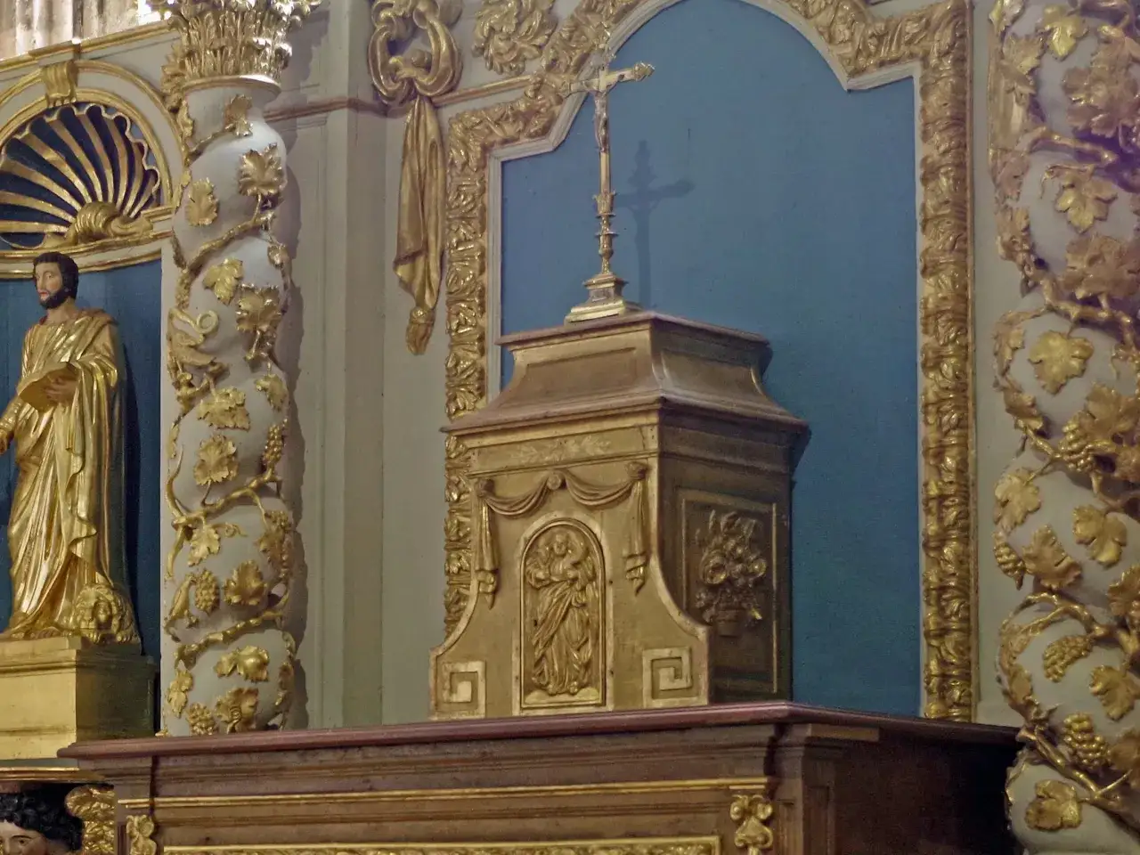 Złoty ołtarz z krzyżem i figurą świętego. Bogate zdobienia w liście winorośli i ornamenty.