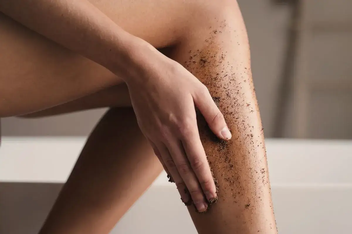 Dłoń rozprowadza peeling na nodze. To idealny peeling przed goleniem, by zapobiec wrastaniu włosków.