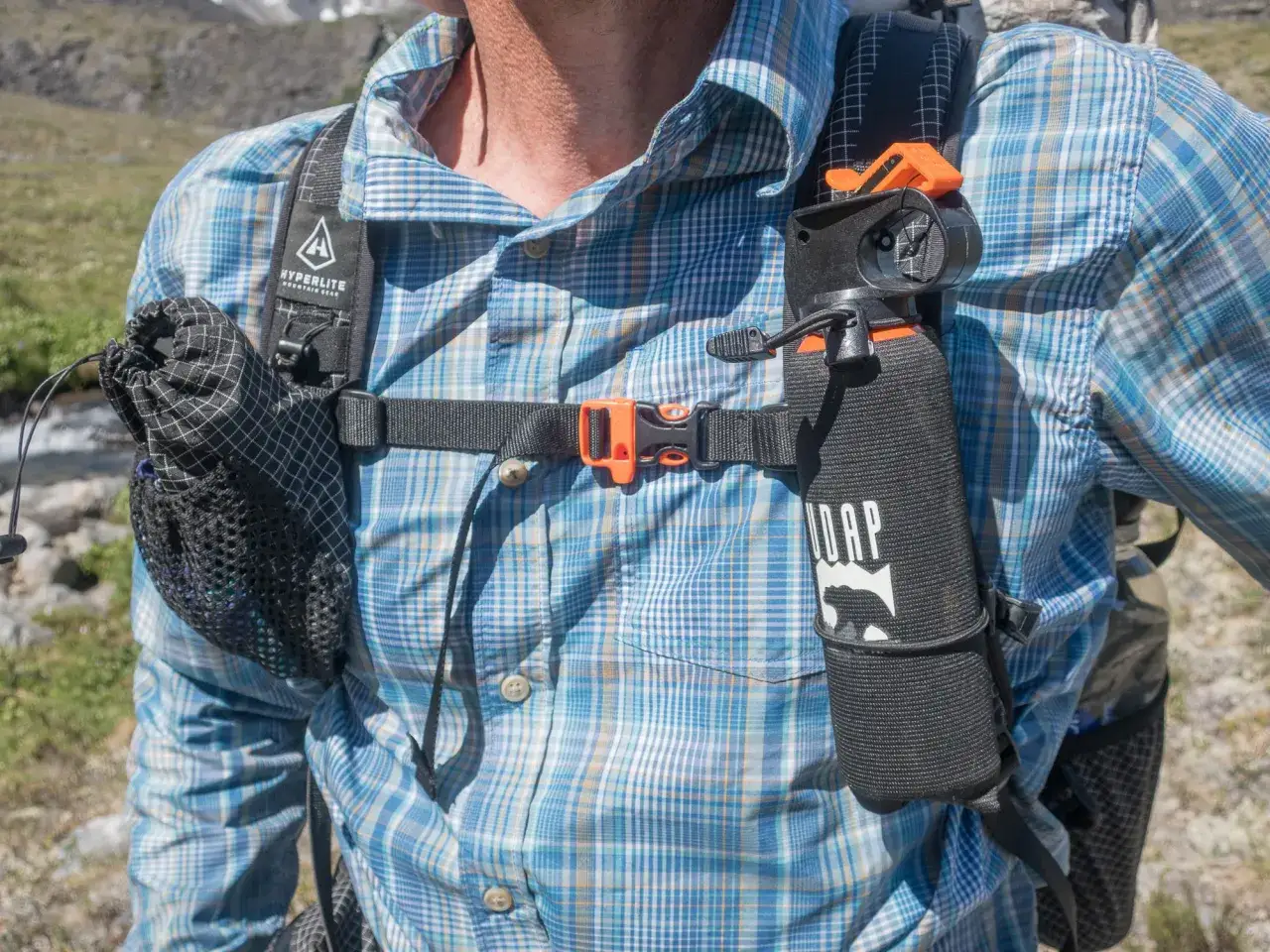 Wanderer befestigt Trinkflasche und Netzbeutel an den Rucksack Schlaufen.