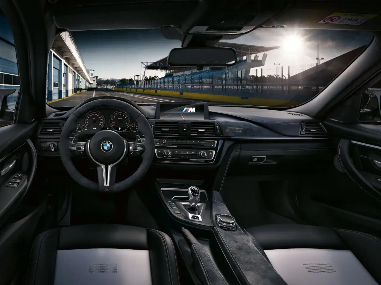 Wnętrze BMW M3 F80 na torze wyścigowym. Widok z perspektywy kierowcy na deskę rozdzielczą, kierownicę i siedzenie.