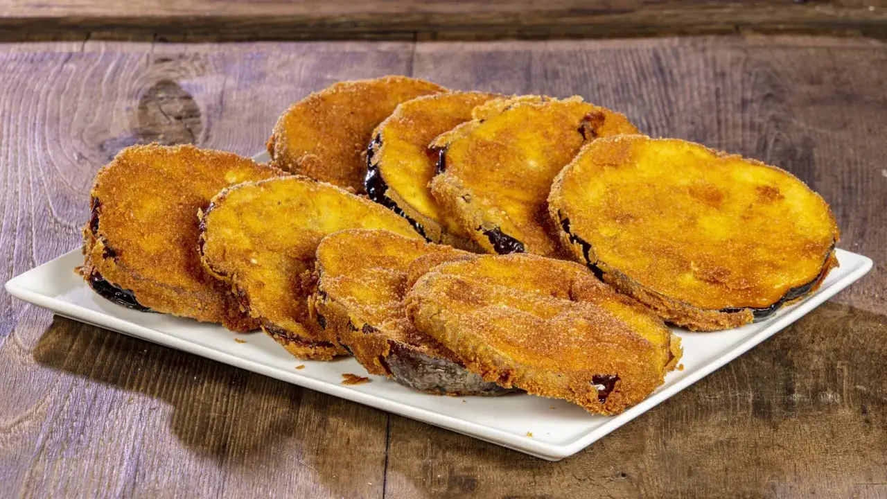 Fette di melanzane dorate e croccanti in padella, impanate con pangrattato, servite su un piatto bianco.
