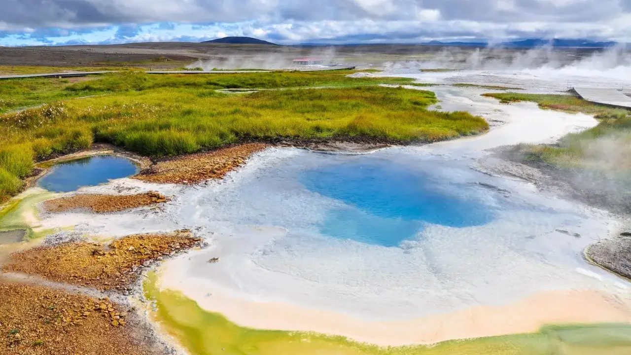 Kolorowe źródła geotermalne w Landmannalaugar na Islandii, z parującą wodą i drewnianymi kładkami.