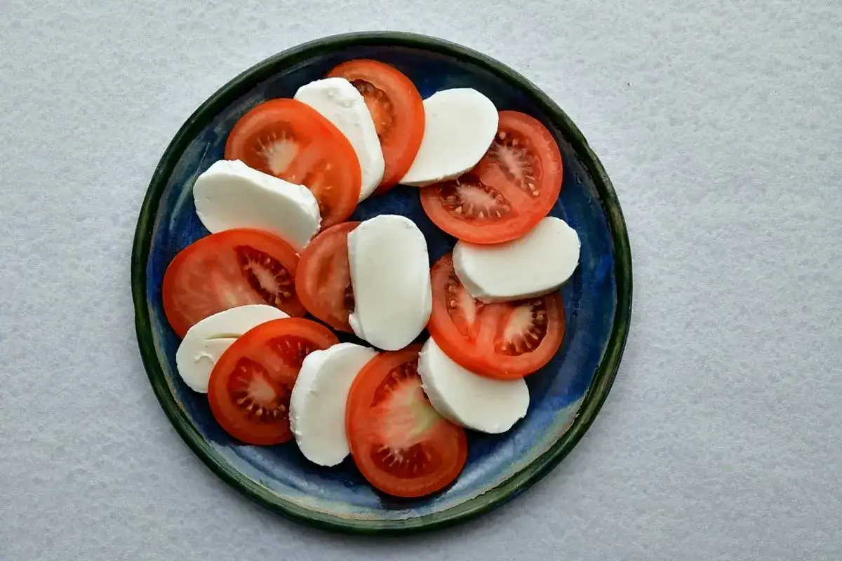 Plasterki pomidora z mozzarellą ułożone na talerzu. Klasyczne połączenie smaków, idealne na lekki posiłek.