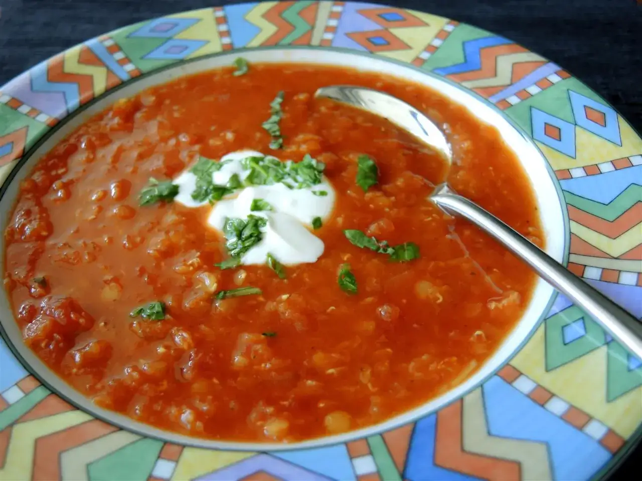 Eine herzhafte italienische Linsensuppe, garniert mit einem Klecks Sahne und frischen Kräutern, serviert in einer bunten Schüssel.