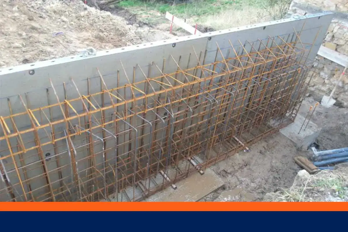 Armature en fer rouillé prête à être coulée dans un mur banché. Le chantier est en cours, la terre est meuble.