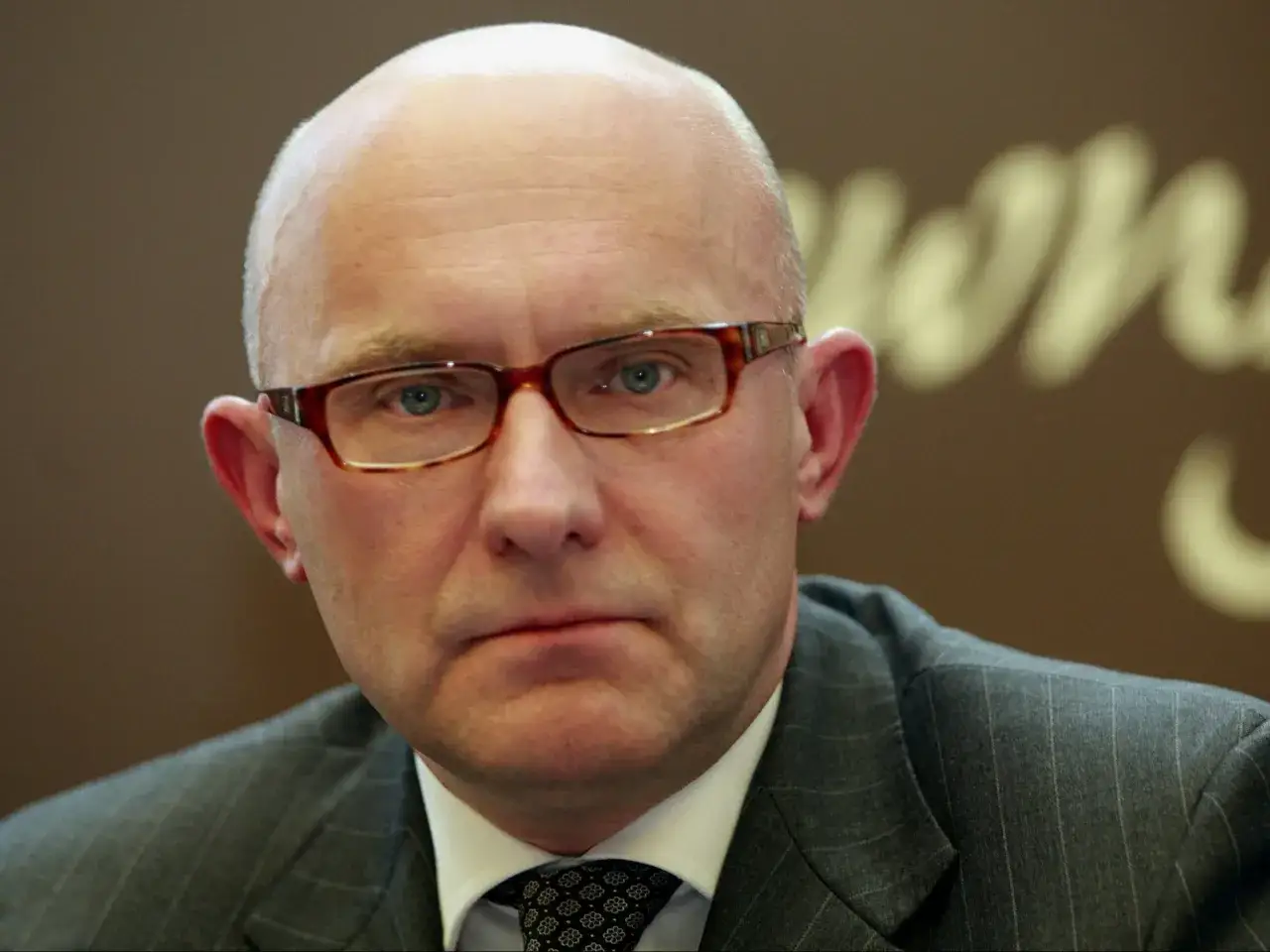 Prezes Orlenu w okularach, w garniturze i krawacie, z uwagą spogląda w obiektyw.