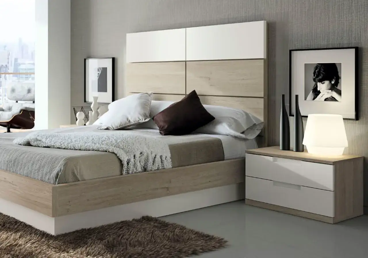 Dormitorio moderno con cama de madera clara y cabecero blanco. Mesita de noche con cajones blancos y l&aacute;mpara. Alfombra mullida.