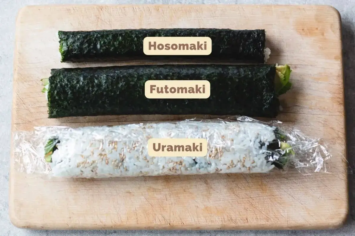 Trzy rodzaje sushi: cienki hosomaki, grubszy futomaki i uramaki z ryżem na zewnątrz, na desce.