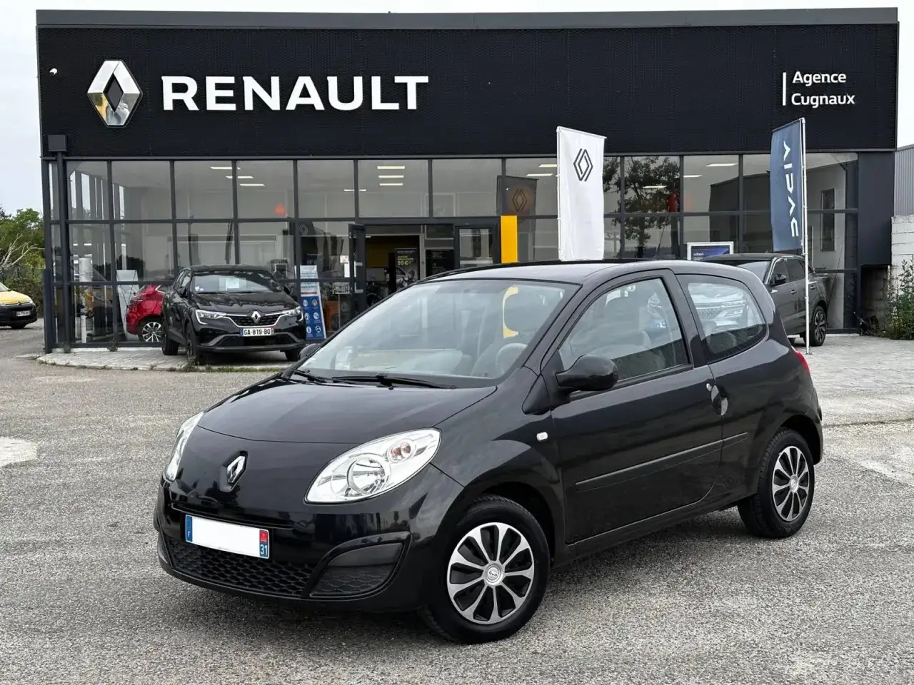 Une Twingo 2 phase 2 noire, prête à partir, devant une concession Renault.