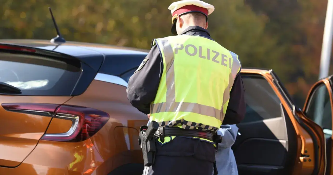 Austriacki policjant w kamizelce odblaskowej przy pomarańczowym samochodzie. Może to oznaczać kontrolę drogową i potencjalne mandaty w Austrii.